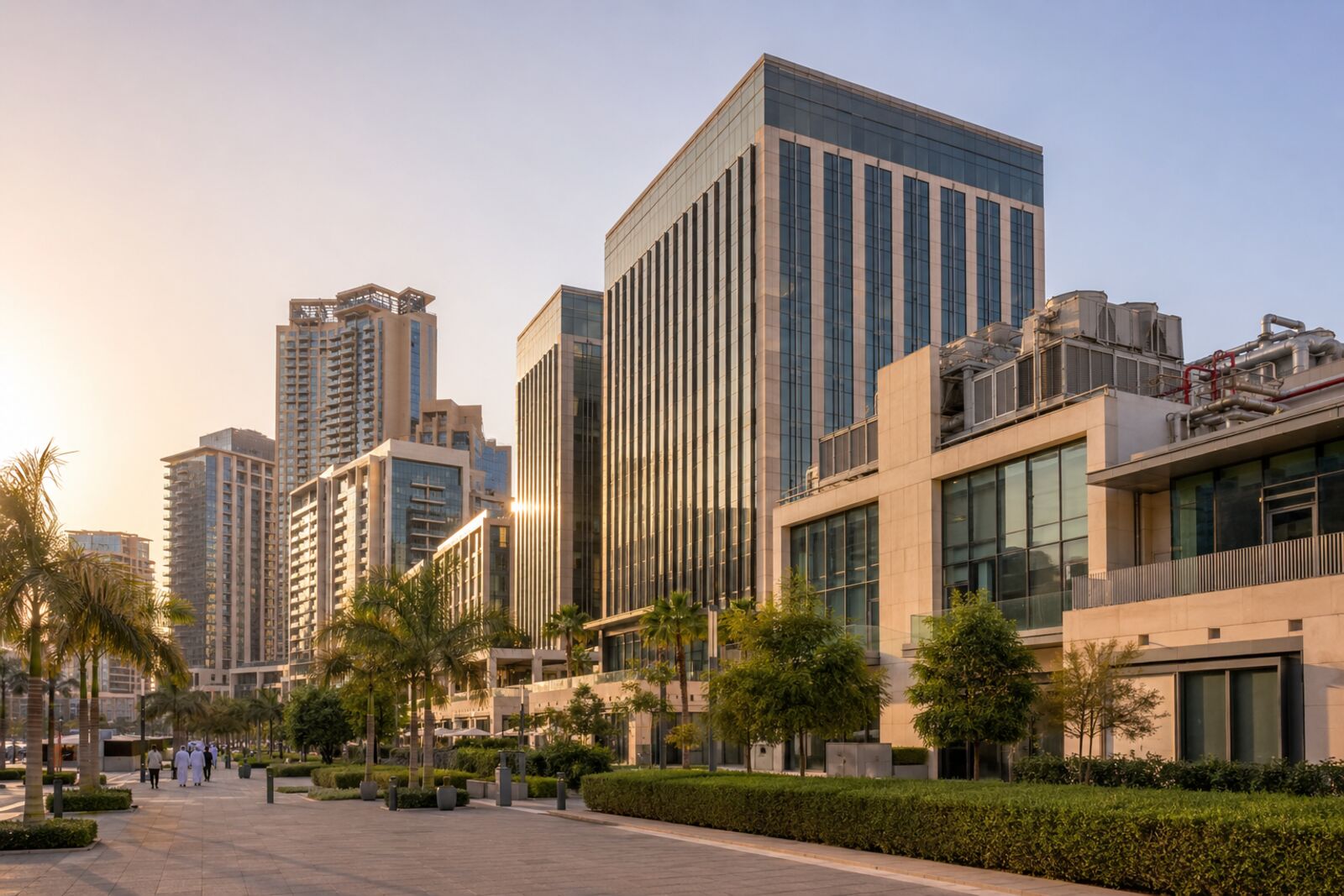 Modern commercial and residential towers in Dubai at sunrise with landscaped walkways and rooftop plant visible